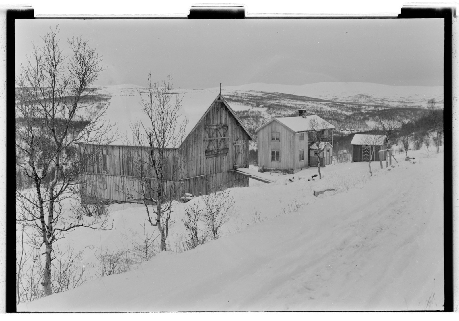 Gårdsbygninger i et snødekt landskap i Hessdalen, fotografert i 1953.